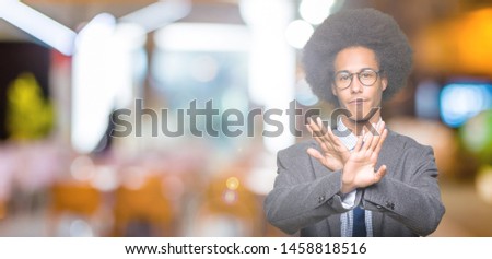 Young african american business man with afro hair wearing glasses Rejection expression crossing arms and palms doing negative sign, angry face