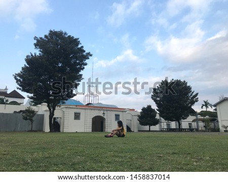 Young teen girl sitting on the grass in front of the old gate.