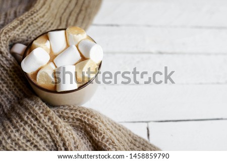 winter flat lay with checkered warm scarf, hot cup of cacao on white wooden background with space for copy.