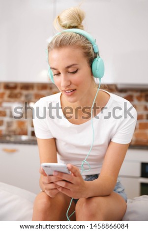Blonde young woman with smartphone and headphones at home.