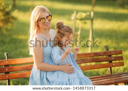 Mom and his little daughter are sitting on a bench in the park