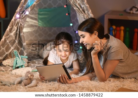 Mother and her little daughter with tablet computer at home in evening Royalty-Free Stock Photo #1458879422