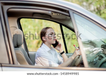 Picture of young businesswoman speaks by phone and doing makeup while driving a car in the traffic jam.