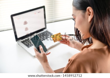 Beautiful asian young woman using credit card with smartphone payment for online shopping in website on laptop