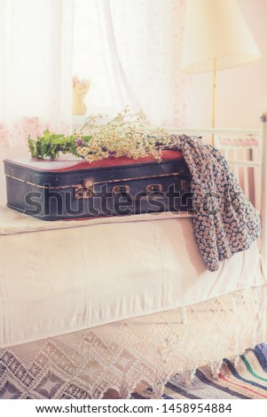 An old suitcase, a bouquet of wildflowers and a simple dress on an old bed. Vintage style, retro photo.
