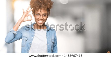 Beautiful young african american woman wearing glasses over isolated background smiling positive doing ok sign with hand and fingers. Successful expression.