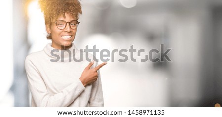 Beautiful young african american woman wearing glasses over isolated background cheerful with a smile of face pointing with hand and finger up to the side with happy and natural expression on face