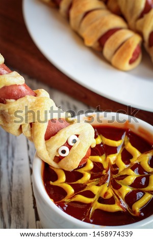 Fun food for kids. Mummy hot dogs held upside down over a bowl of ketchup and mustard dip, with spider web design. 