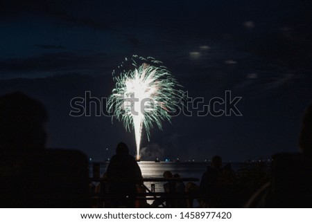 Fireworks over water on a lake as people watch the show on a summer night