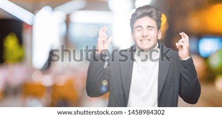 Young elegant man wearing winter coat over isolated background smiling crossing fingers with hope and eyes closed. Luck and superstitious concept.