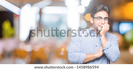 Young handsome man wearing glasses over isolated background looking stressed and nervous with hands on mouth biting nails. Anxiety problem.