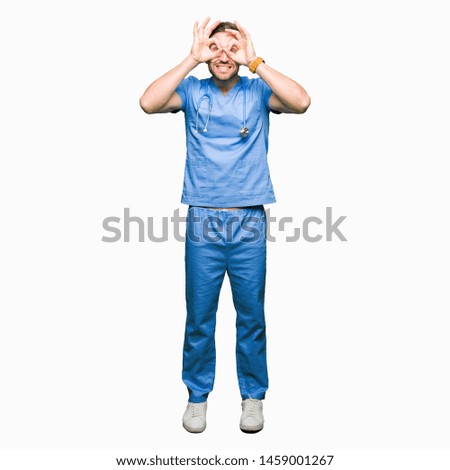 Handsome doctor man wearing medical uniform over isolated background doing ok gesture like binoculars sticking tongue out, eyes looking through fingers. Crazy expression.