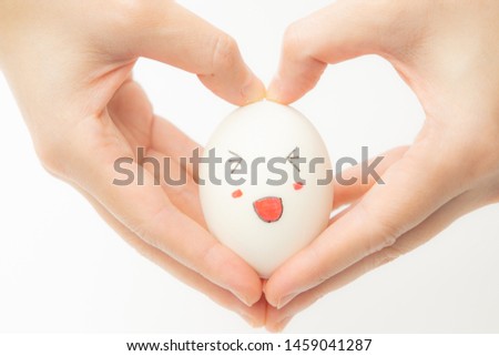 Give love concept. A white egg laying on the heart-shaped hand. On the egg, drawing a happy smile. White background.