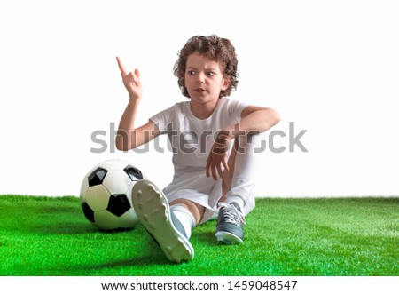 Puzzled little footballer sitting on the grass. Copy space