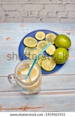 View of a pitcher of lemonade with ice next to some slices of lemon and lime
