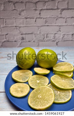 view of whole limes and slices of fresh lime on a blue plate
