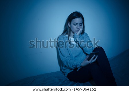 Young teenager girl suffering mobile cell phone addiction feeling lonely and depressed having insomnia needing to be connected sitting on bed late at night. In Royalty-Free Stock Photo #1459064162