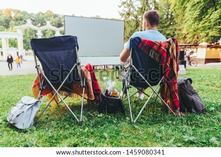 man sitting in camp-chair in front of open air cinema screen eating chips leisure time