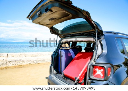 A woman in a hat and sunglasses and a black car on the sandy beach. Blue ocean and sky in distance.