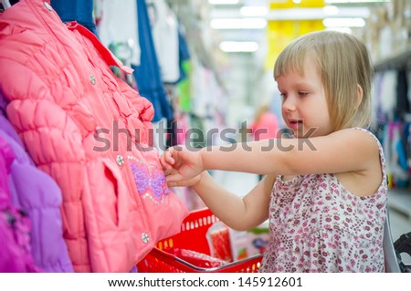 Adorable girl select winter jacket in cloth department in supermarket