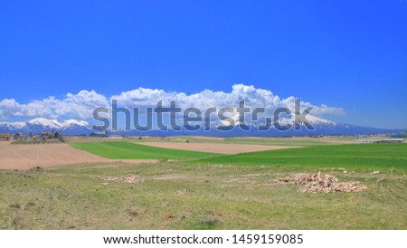 The photo was taken in Turkey on the high plateau of Cappadocia. The picture shows green agricultural fields on the background of snowy mountain peaks.
