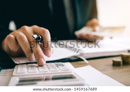 Investors are calculating on calculator investment costs and holding cash notes in hand. Royalty-Free Stock Photo #1459167689