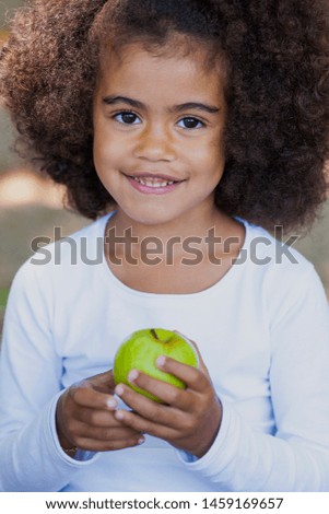Mixed race little girl outside with green apple.