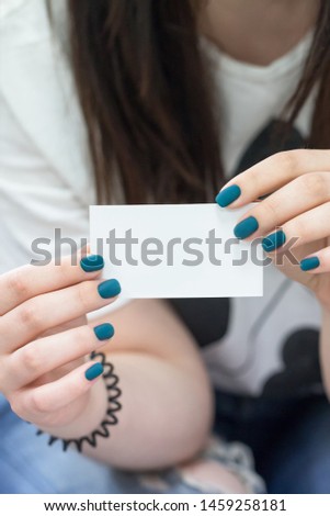 Female hands holding white empty business card. Manicure with turquoise blue nail polish