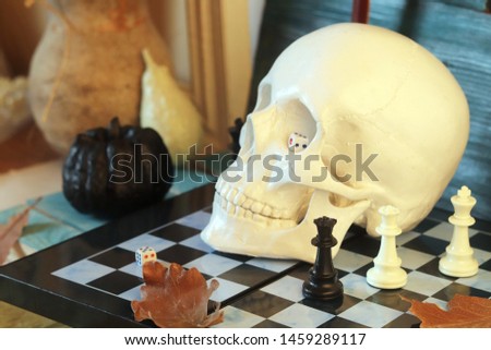 Decorative composition of a skull, pumpkins, frames and mystical decor on a chessboard with figures, on a wooden table, a dark background, interior design for Halloween, autumn, October