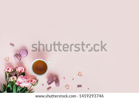 Pink background with macaroons and a Cup of tea surrounded by peonies. Top view with space for your text.