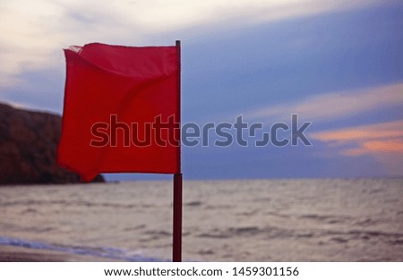 Red flag on the beach, sea and blue cloudy stormy sky in the background