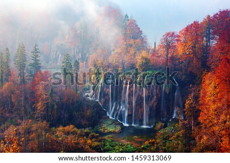 Incredible view on foggy waterfall in Plitvice lakes. Orange autumn forest on background. Plitvice National Park, Croatia. Landscape photography