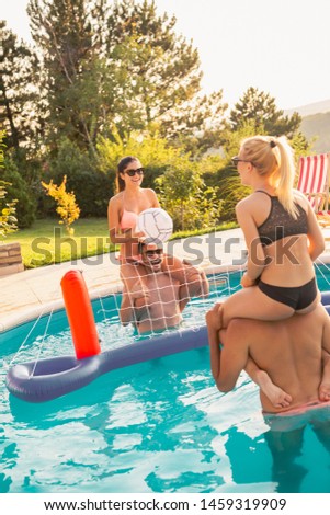 Two young couples having fun at a summertime poolside party, playing volleyball in the swimming pool