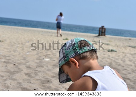 little boy. sitting on beach. silhouette of mother on background