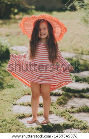 Cute baby girl with long hair in a striped dress with a pink hat. Concept of holidays, summer fan, girls fashion.