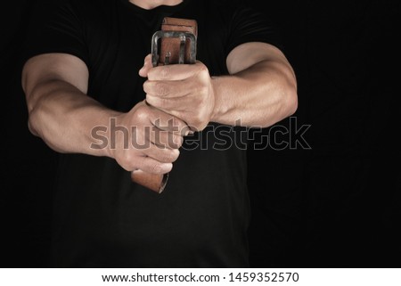adult man in black clothes holding a brown leather belt with an iron buckle, concept of  aggression