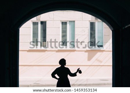The concept of fashionable summer, blue and green colors. Stylish young woman in blue beret and skirt with a green shirt is standing on the street in the arched doorway silhouette close view