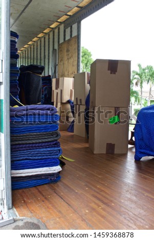 Moving van interior with packed boxes by open door with bright identity labels or writing on each to identify what room they go to. movers use dollies and hand trucks on loading ramp for furniture and