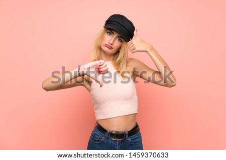 Young blonde woman with hat making good-bad sign. Undecided between yes or not