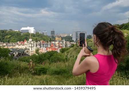 Girl in a red dress with coffee in hand makes a photo of a beautiful panorama of the city on her mobile phone