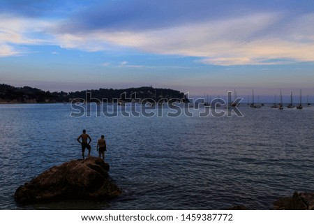 View of the beach, two bathers on a rock, bay of Beaulieu sur Mer, Saint Jean Cap Ferrat at sunset