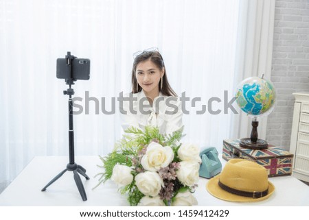 Young Asian woman as vlogger or blogger attending video conference at desk in office.