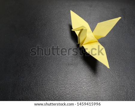 Origami Crane On Dark Background. Yellow origami paper crane on 
black background with copy space. Paper bird on the table.