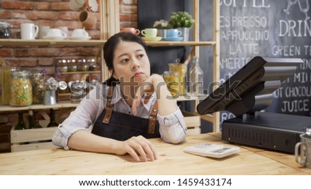 bored waitress girl in apron sitting in cafe bar counter with hand in chin looking out store. depressed coffee shop owner with no customer visiting. unhappy lady worried about small startup business Royalty-Free Stock Photo #1459433174
