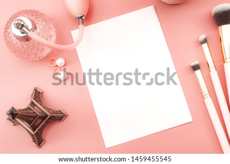 Nostalgia concept theme with ornamental set with miniature replica of Eiffel tower, vintage bottle of perfume, makeup brushes and earrings isolated on pink background with copy space on blank paper