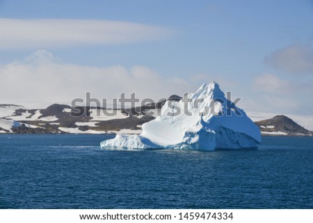 An iceberg shaped like a mountain floating on waters with Antarctic shorelines in the background.