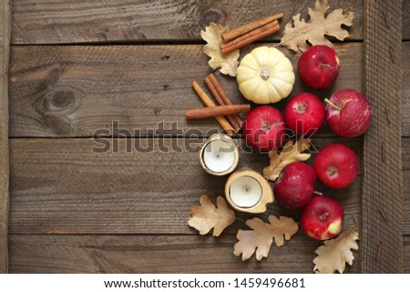Autumn composition of red apples, dry oak leaves, cinnamon sticks, pumpkin and candles on rustic weathered wood. Top view, flat lay.
