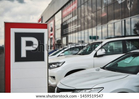 A parking sign at a car dealership close-up and the cars behind it.