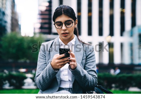 Latino businesswoman checking mobile notification on modern cell smartphone, Hispanic female CEO using digital phone for search contact number or data info during work break at urban setting