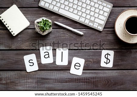 Office desk with notebook, sale word and dollar sign on wooden background top view